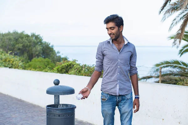 Man throwing trash in recycling bin, isolated outside seaside tropical background. Recycling, eco friendly approach concept. Keep streets, city, earth clean