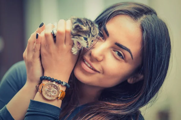 Pets Care.Young woman holding cat home. Closeup striped Cute cat in woman hands. Focus on girl, kitty out of focus