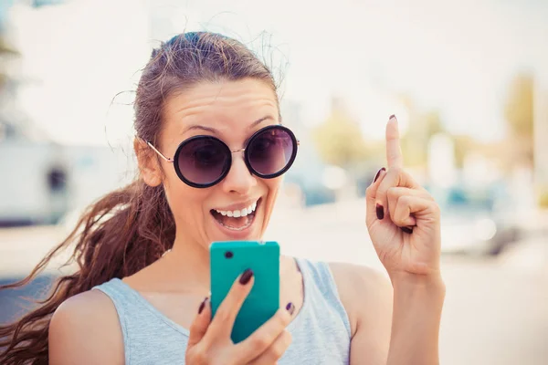 Щаслива дівчина має ідею вказуючи на жест пальця, дивлячись на телефон — стокове фото