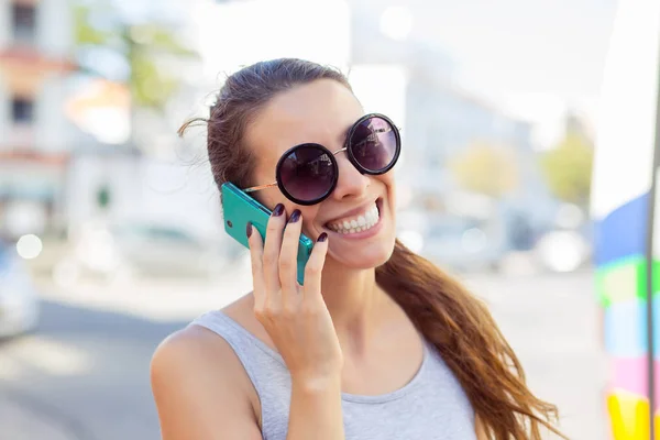 Mulher eufórica conversando com seu telefone inteligente em uma estação de ônibus enquanto espera — Fotografia de Stock