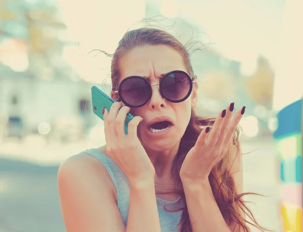 Porträt einer wütenden jungen Frau, die auf ihrem Handy schreit und draußen vor dem Hintergrund der Stadt steht. Negative Gefühle — Stockfoto