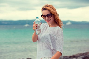 İçme suyu ve plajda bir deniz arka plan üzerinde çalıştırdıktan sonra serinlemek güneş gözlüğü güzel genç esmer kadın. Uygulanan Instagram filtre efekti 