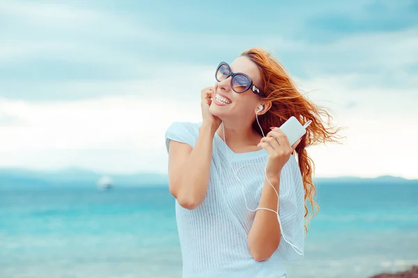 Πορτρέτο του ένα χαμογελαστό κορίτσι με ακουστικά μουσική σε εξωτερικούς χώρους από την παραλία με φόντο του ουρανού μπλε του ωκεανού — Φωτογραφία Αρχείου