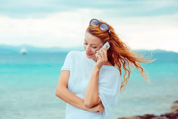 Wanita muda yang bahagia berbicara di telepon genggam di pantai dengan latar belakang laut, Sardinia Italia — Stok Foto