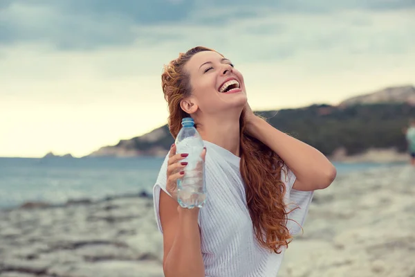 Feliz chica sonriente y saludable bebiendo agua. hermosa joven disfrutando de la naturaleza sosteniendo botella de agua — Foto de Stock