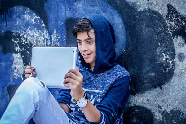 Feliz adolescente sonriente mirando en su almohadilla leyendo noticias viendo películas aisladas al aire libre graffiti wall — Foto de Stock