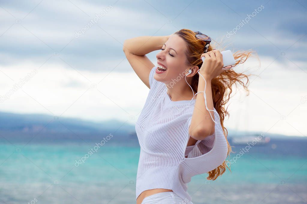 happy woman arms in air enjoying nature dancing listening to the music outdoors sea background