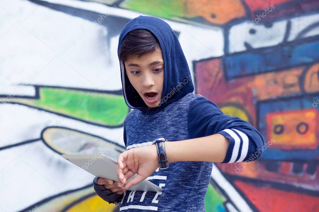 Boy, man with tablet pad running late to school looking to wrist watch over graffiti wall