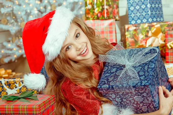 Młoda dziewczyna szczęśliwy w Boże Narodzenie kapelusz uśmiechający się gospodarstwa prezent — Zdjęcie stockowe