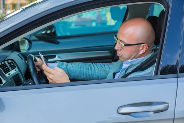 Man Distracted guy in car with mobile phone texting while driving. Side view. — Stock Photo, Image