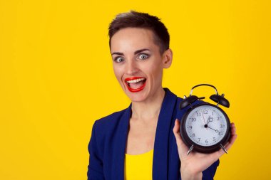 Anticipation. Headshot young funny looking excited business woman holding alarm clock waiting isolated yellowwall background. Human face expressions emotions. Time punctuality busy schedule concept clipart
