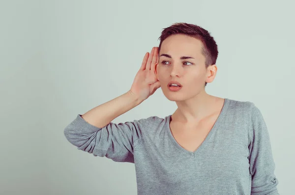 La mujer sostiene su mano cerca de la oreja y escucha cuidadosamente aislada sobre un fondo de pared gris verdoso. Emoción humana, expresión facial — Foto de Stock