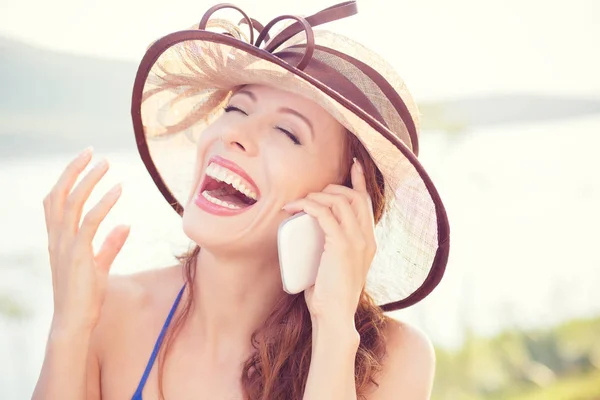 Mulher eufórica falando com seu telefone inteligente ao ar livre fundo. Senhora de chapéu rindo de celular — Fotografia de Stock
