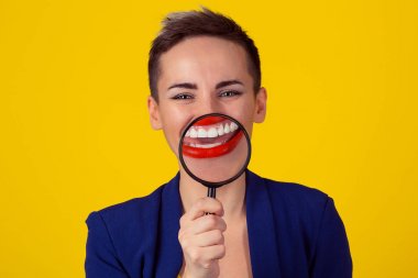 Beyaz sağlıklı ağız diş kavramı. Tatlı beyaz dişler Büyüteç izole sarı arka plan duvar aracılığıyla gösterilen gülüyor gülümseyen iş takım elbiseli, mutlu kadın portre. Kız kırmızı dudaklar kısa saç