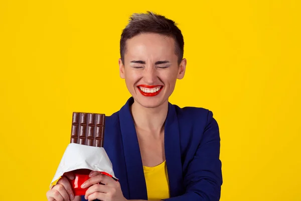 Mujer con chocolate riéndose. Primer plano retrato mujer joven labios rojos riendo comer chocolate chocolate barra ojos cerrado feliz aislado fondo amarillo pared —  Fotos de Stock