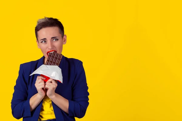 女人累的渴求糖果巧克力的饮食限制。特写肖像女孩吃咬巧克力棒孤立的黄色背景墙 — 图库照片