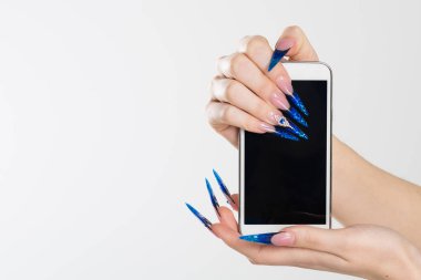 Kadın el telefon tutarak stiletto çivi ile. Sanat manikür. Modern stil mavi oje. Mobil cep telefonu holding güzellik eller. Şık renkli stiletto izole beyaz arka plan çivi