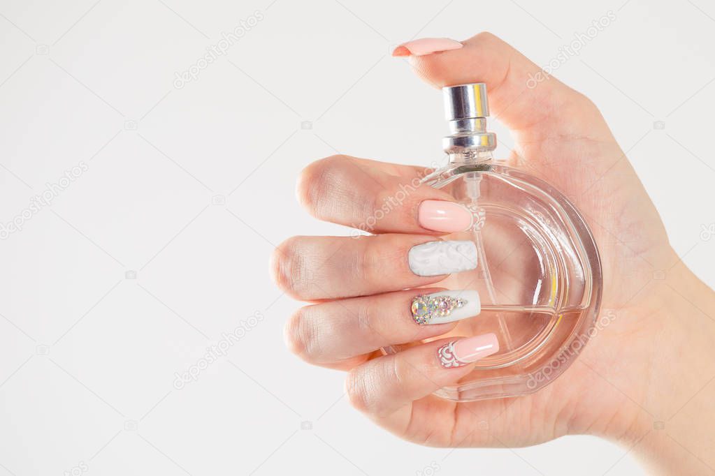 Closeup nail polished pastel multicolored nails coral pink, white with crystals, hand holding perfume bottle isolated on white grey background wall. Classic wedding bride nails design