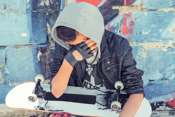 Sad crying Teenager boy with skateboard in city over blue red gr — Stock Photo, Image