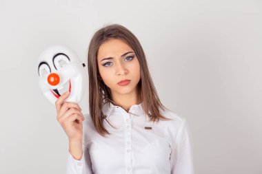 Genç portre endişeli kadın üzgün ifade beyaz duvar arka plan üzerinde izole neşe mutluluk ifade bir palyaço maskesi holding ile üzgün. İnsan yüz ifadesi duygu