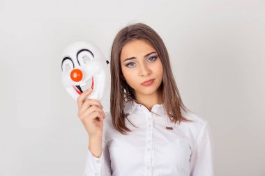 Şüpheli içeride. Bir maske takıyor. Beyaz arka plan portre genç şüpheli endişeli kadın şüpheci ifade kameraya bakarak neşe mutluluk ifade bir palyaço maskesi holding ile izole.