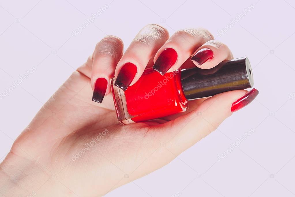 Woman holding bottle of nail polish. Nail Polish. Art Manicure. Modern style red black Nail Polish. Stylish Colorful stiletto Nails isolated pink background. Beautiful female hand with beauty manicure