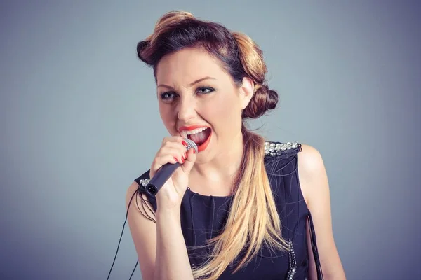 Singer. Sexy brunette long hair singing into microphone isolated blue grey background wall — Stock Photo, Image