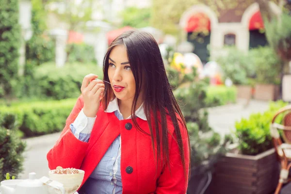 Закрыть портрет молодой женщины, поедающей мороженое, облизывающей ложку на открытом воздухе в кафе на летней террасе. Вид сбоку — стоковое фото