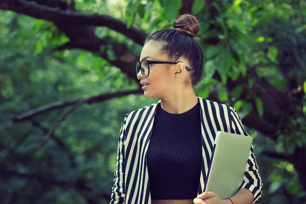 Student woman in profile holding laptop looking to the side in park