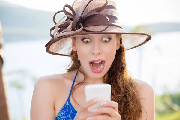 Gros portrait surpris criant jeune fille en chapeau regardant le téléphone voir des nouvelles ou des photos avec une émotion drôle sur son visage isolé en dehors de l'arrière-plan de la ville. Émotion humaine, réaction, expression — Photo