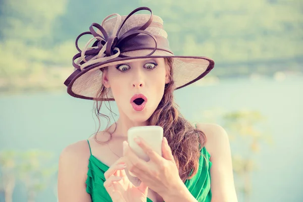Närbild porträtt förvånad ung kvinna i hatt tittar på telefonen ser oväntade nyheter eller bilder med konstigt känsla på hennes ansikte utanför staden. Mänskliga känslor, reaktion, uttryck — Stockfoto