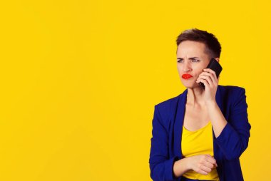 Portre portre kızgın genç kadın, hoş olmayan, kötü konuşmayı cep telefonuyla konuşan genç sarı duvar arka plan izole. Negatif insan duyguları, yüz ifadeleri, tepki, duygular