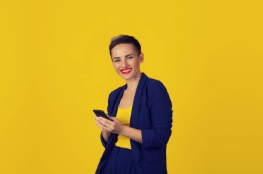 Seni kameraya gülümseyen izole üzerinde sarı duvar bakarak akıllı cep telefonu kullanarak tutan eller tatlı kadın. Yeni nesil teknolojileri bağımlılığı konsept telefon. Müşteri hizmet sağlayıcı ilişkisi