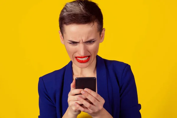 Плохие новости. Портрет злобной безумной угрызения совести молодой женщины, смотрящей на мобильный телефон, изолированный на желтом фоне. Отрицательные человеческие эмоции — стоковое фото