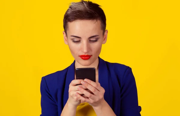 Mujer de negocios seria mirando mensajes de texto en el teléfono aislado pared de fondo amarillo. Pelo corto, desgaste formal — Foto de Stock