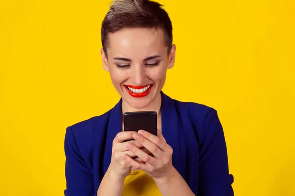 Mantenerse conectado. Mujer joven feliz mirando su teléfono móvil y sonriente puño de bombeo celebra el éxito aislado fondo amarillo de la pared. Emocionada chica riendo recibiendo buenas noticias en el teléfono celular — Foto de Stock