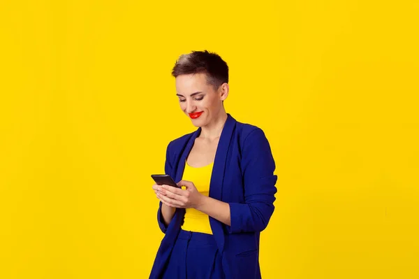Perfil lateral del retrato de primer plano mujer sonriente utilizando la aplicación en un teléfono inteligente aislado en el fondo amarillo de la pared — Foto de Stock