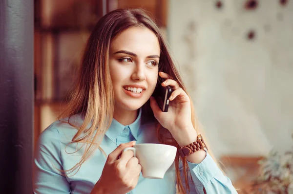 携帯電話の話。カフェ都市生活に笑顔の女性電話屋内のおしゃれなトレンディな都市のカフェに座っているスマート フォンのアプリでテキスト メッセージのテキスト メッセージを話しているコーヒーを飲む. — ストック写真
