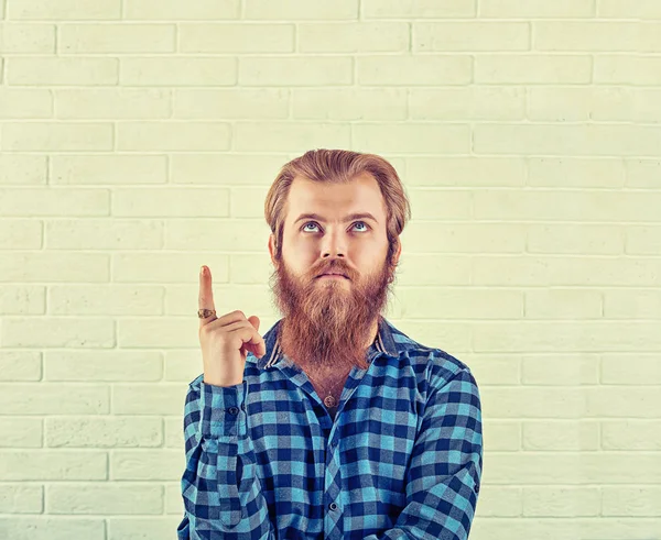 Ritratto di un premuroso uomo camicia blu casual che punta il dito verso l'alto isolato su uno sfondo bianco muro di mattoni. Immagine di colore giallo, orizzontale. Emozione umana neutra, espressione facciale — Foto Stock