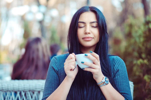 Люблю кофе. Портрет милой девушки, пьющей чай на балконе над открытой террасой с зеленым кустарниковым фоном, в голубой серой блузке и завтракающей, с удовольствием расслабляющей — стоковое фото