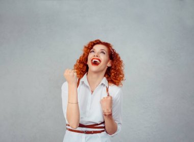 Winner. Happy redhead curly woman exults pumping fists ecstatic celebrates success hands gesture isolated on gray background. Positive human emotion, face expression, body language, attitude clipart