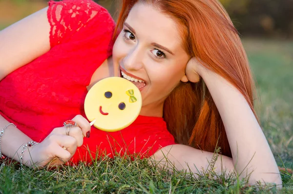 Mujer comiendo una piruleta y sonriendo acostado en césped de hierba verde — Foto de Stock