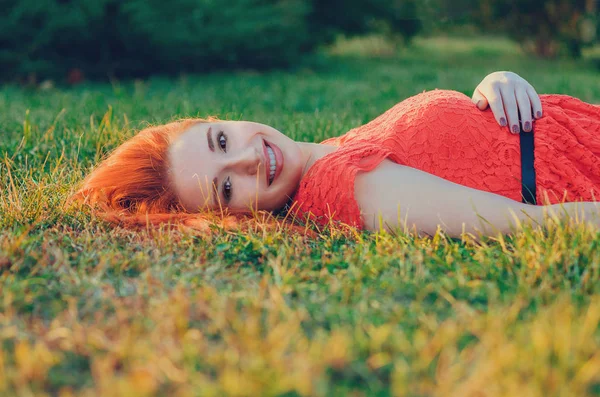 Jonge inhoudsmodel met rode hoofd lange haren liggen op gras in de zomer park glimlachen — Stockfoto