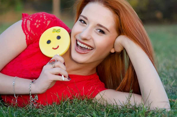 Encantadora chica con dulces de azúcar se encuentra en la hierba verde y se ríe felizmente — Foto de Stock