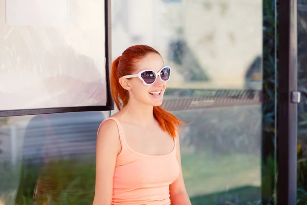 La chica sentada en la parada de autobús en gafas de sol esperando el autobús — Foto de Stock