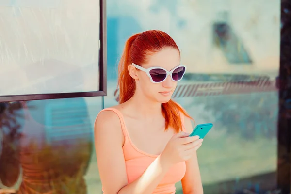Mulher menina do sexo feminino sentado em uma estação de ônibus usando o aplicativo no smartphone para chamar táxi — Fotografia de Stock