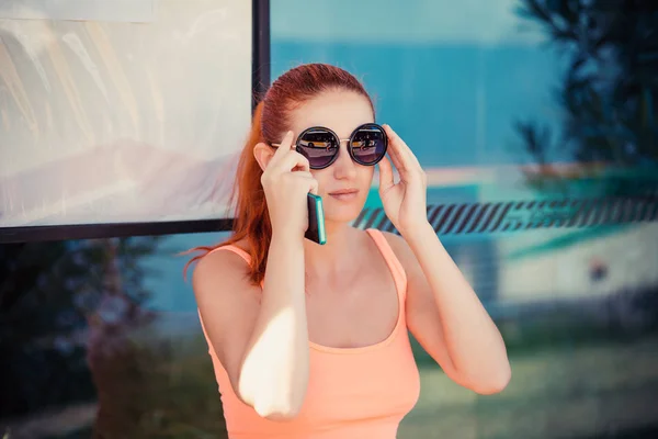 Mujer chica sentada en una estación de autobuses ajustando gafas de sol redondas — Foto de Stock