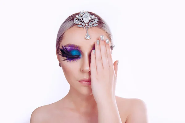 Женщина красота с художественным фиолетовым голубыми глазами макияж перо на ресницы серебряные украшения на голове покрывает половину лица рукой — стоковое фото