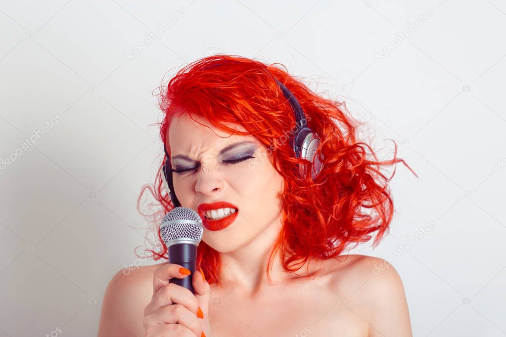 Portrait of beautiful young woman in headphones singing into a microphone
