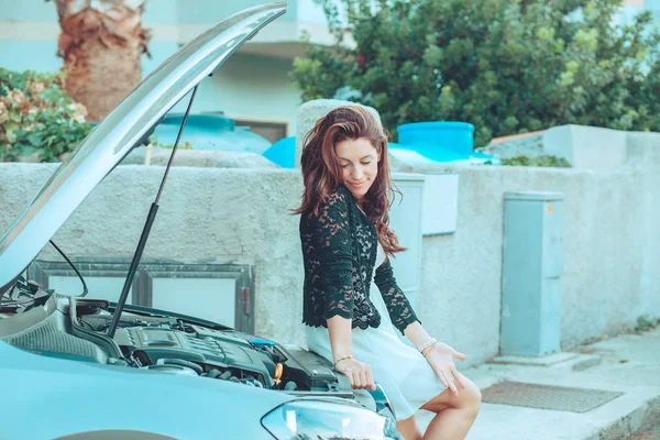 Жінка сидить на відкритій машині, дивлячись на двигун у відкритій витяжці розчарована — стокове фото